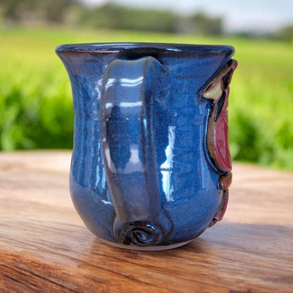 Blue ceramic mug with a unique design on a wooden surface with a grassy background