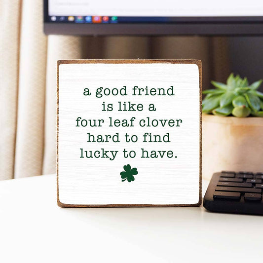 Decorative sign with a four-leaf clover and text on a desk.
