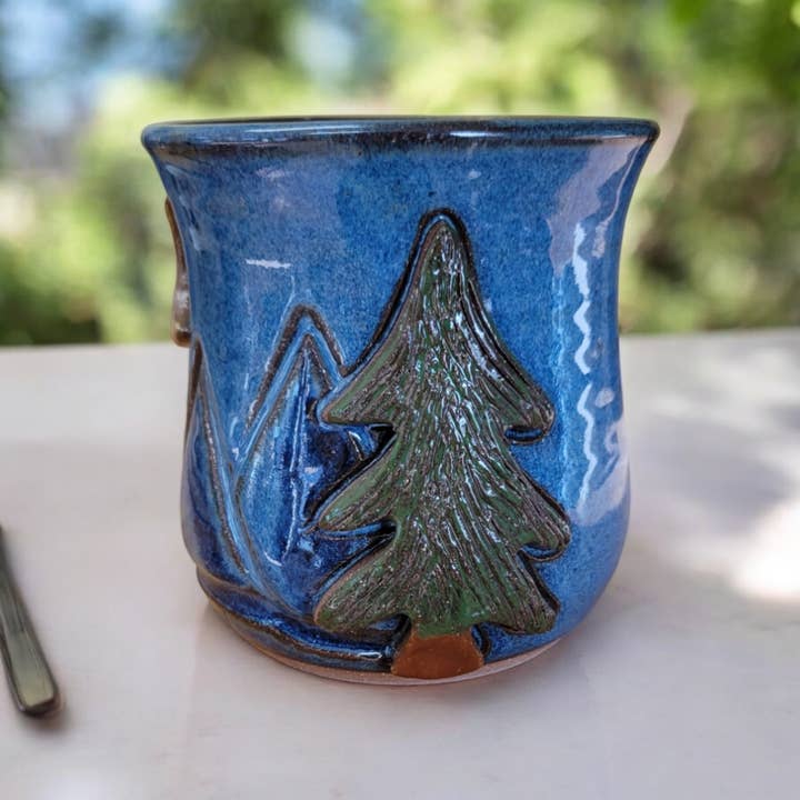 Blue ceramic mug with a tree design on a white surface