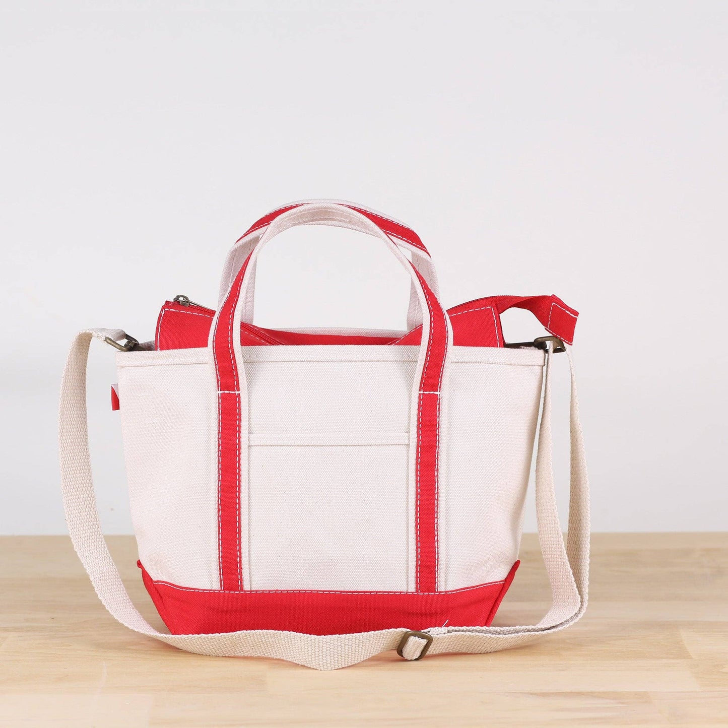 White tote bag with red accents on a wooden surface and light gray background