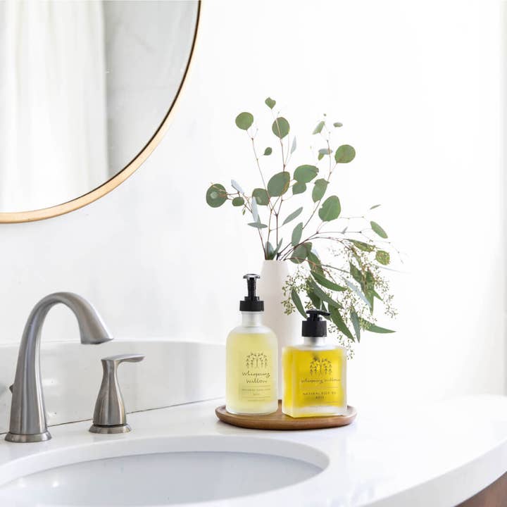 Bathroom sink with two bottles of soap, a vase with greenery, and a mirror.