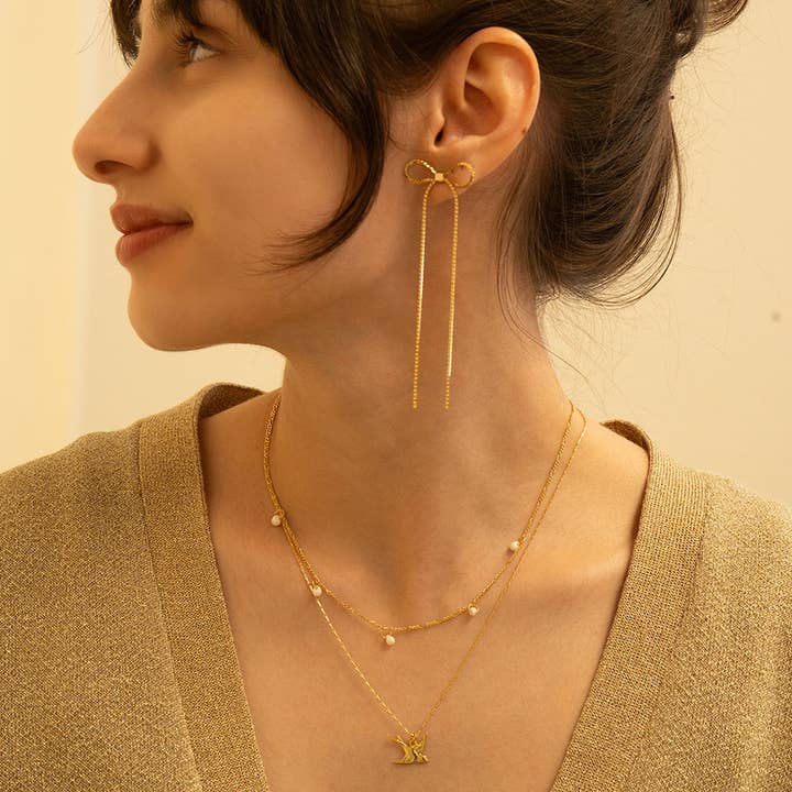 Woman wearing gold earrings and necklaces against a neutral background