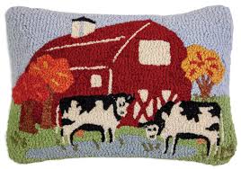 A rectangular hand-hooked wool pillow featuring a farm scene with a red barn, black-and-white cows, green grass, and autumn trees on a light blue background.