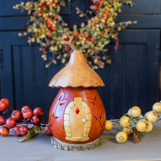 Decorative gourd with a small door on a surface with autumn decorations in the background.