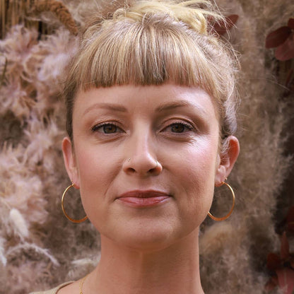 Woman with styled hair and hoop earrings against a floral background