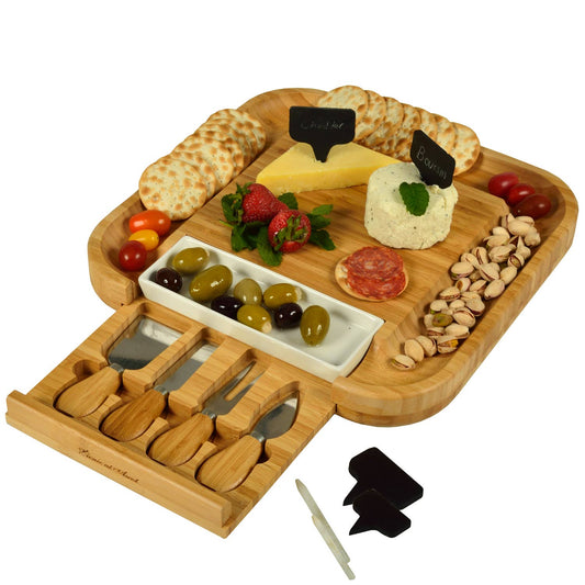 Wooden charcuterie board with assorted foods and cheese tools on a white background