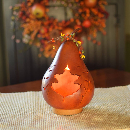 Decorative gourd luminary with cut-out design on a table with a fall-themed wreath in the background.