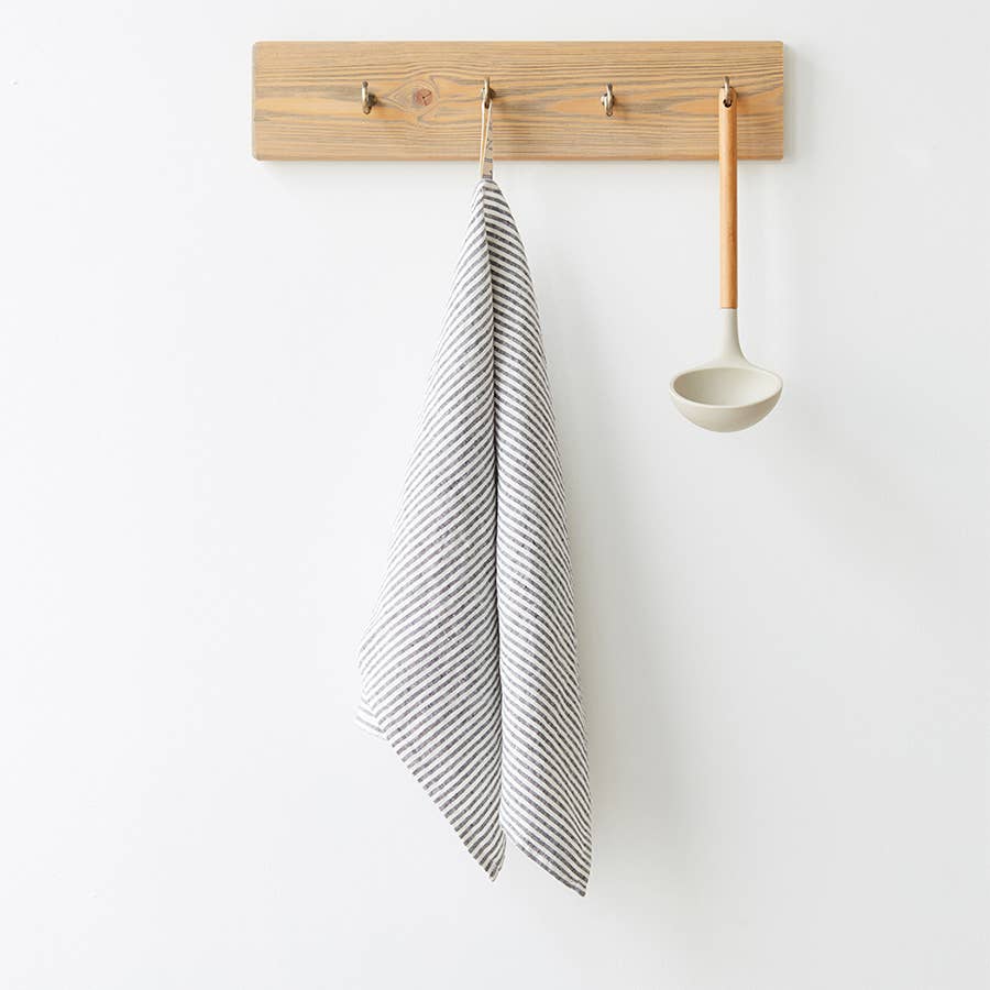 Striped towel and ladle hanging on a wooden wall hook against a white background