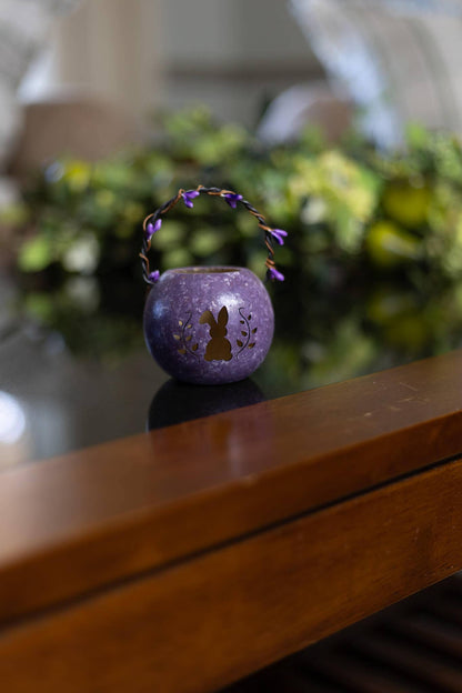 Purple decorative lantern with a rabbit design on a wooden surface with blurred greenery in the background