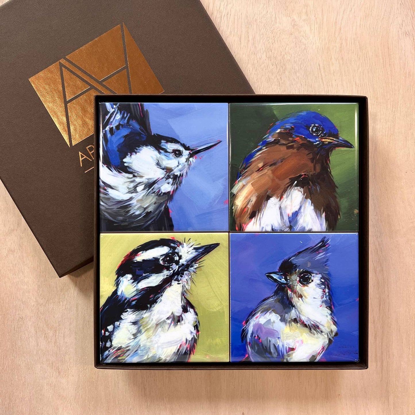 Set of four bird-themed coasters in a decorative box on a wooden surface