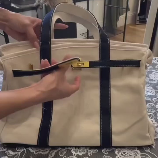 Hands demonstrating the interior flap closure on a navy canvas boat tote, showing how the bag closes securely at the top