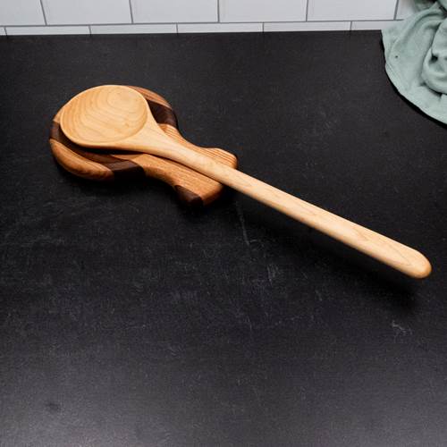 Wooden spoon on wooden spoon rest on top of a black surface with a tiled wall background.