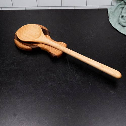 Wooden spoon on wooden spoon rest on top of a black surface with a tiled wall background.