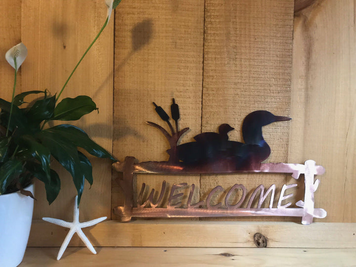 Decorative metal welcome sign with loons on a wooden wall