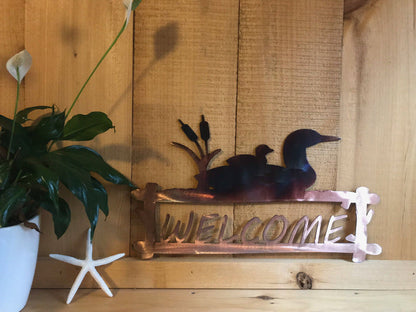 Decorative metal welcome sign with loons on a wooden wall