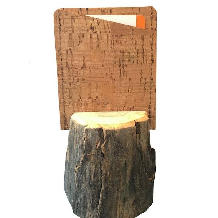 A cork card holder wallet held up by a wooden stand on a white background.