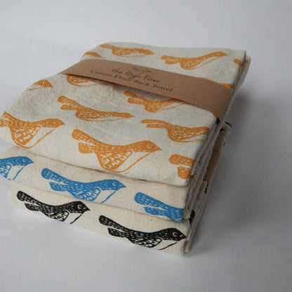 Stack of folded cotton tea towels with bird print, packaged with a brown paper band displaying the brand name 'The High Fiber'.