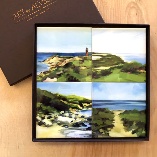 A set of four ceramic tile coasters with cork backing, each featuring a different image of a beach scene, presented in a brown gift box with 'Art by Alyssa' logo foil stamped on the top.