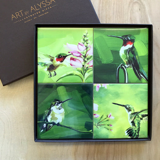 A set of four ceramic tile coasters with cork backing, each featuring a different image of hummingbirds, displayed in a high quality gift box with 'Art by Alyssa' logo.