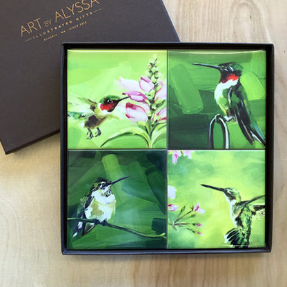 A set of four ceramic tile coasters with cork backing, each featuring a different image of hummingbirds, displayed in a high quality gift box with 'Art by Alyssa' logo.