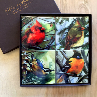 A set of four ceramic tile coasters with cork backing, each featuring a colorful bird painting, displayed in a gift box with 'Art by Alyssa' branding.