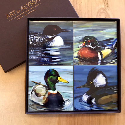 A set of four ceramic tile coasters with cork backing, each featuring a different image of waterfowl from original oil paintings, packaged in a gift box with 'Art by Alyssa' branding.