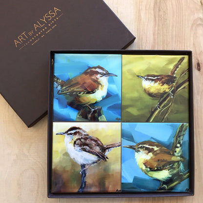 A set of four ceramic tile coasters with cork backing, each featuring a colorful painting of a wren bird, displayed in a black gift box with 'Art by Alyssa' logo.