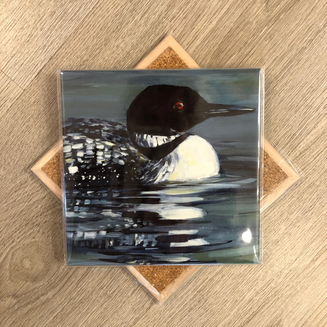 A square ceramic trivet with an image of a loon bird on water, surrounded by a cork backing.