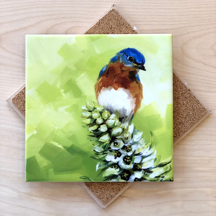 A 6-inch square tile trivet with an image of a bluebird perched on flowers, featuring a green background, with cork backing.