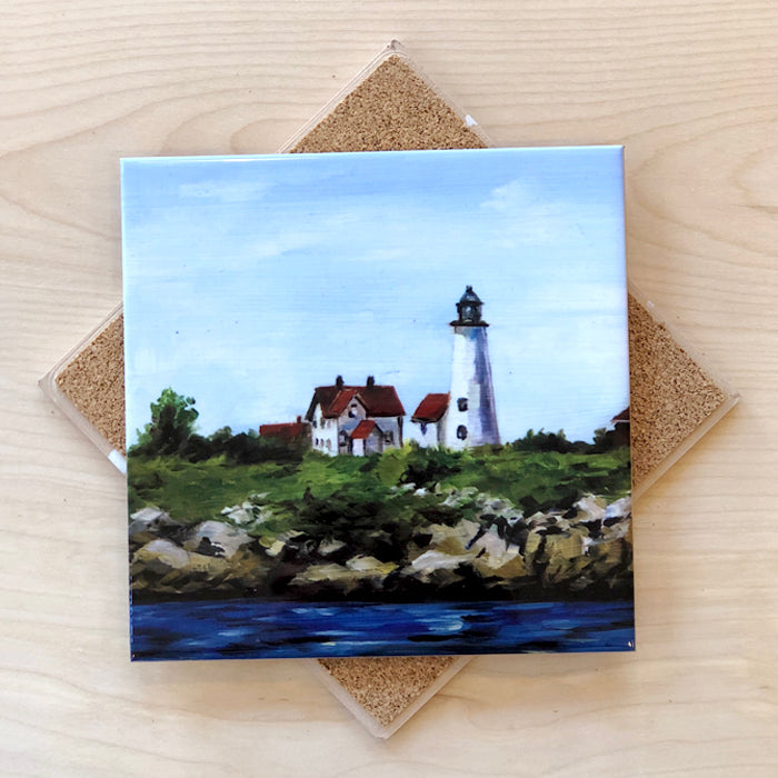 A square ceramic trivet with a cork backing, featuring an image of a lighthouse on a clear blue sky background.