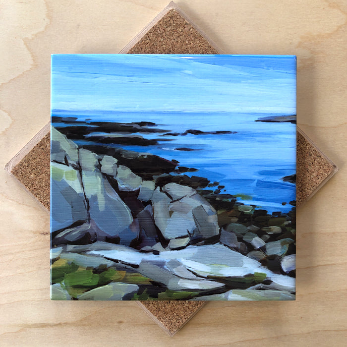 A square ceramic trivet with a cork backing featuring an artistic depiction of a pebble beach scene in blue and green colors.