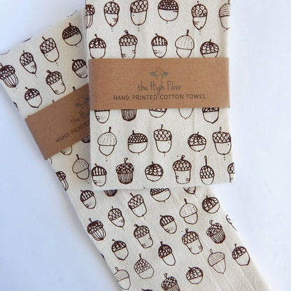 Two beige cotton tea towels with brown acorn prints, wrapped with a brown paper band displaying the brand name 'The High Fiber'.