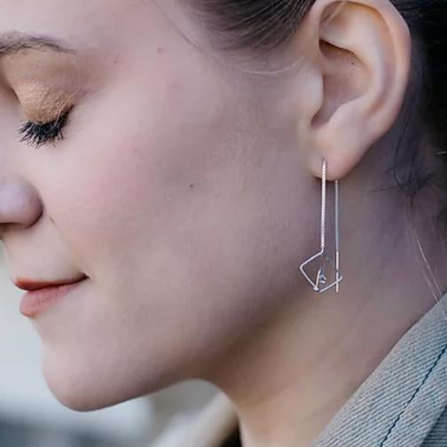 A person wearing a silver earring with a geometric threader design.